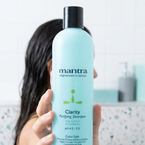 Woman holding a bottle of Mantra Clarity Purifying Shampoo up to the camera in a bright bathroom