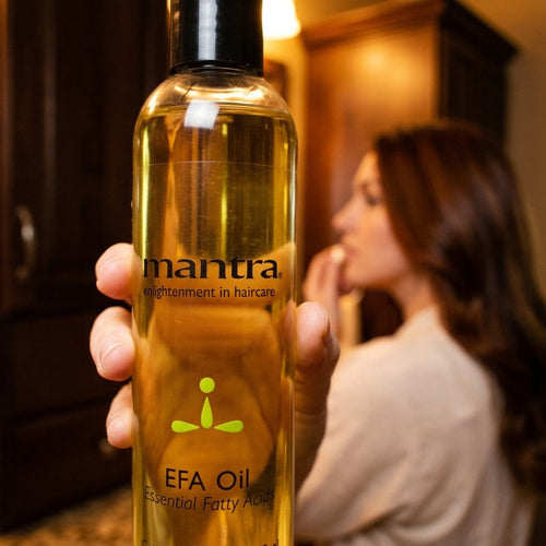 Woman with glossy colour-treated hair holding a bottle of Mantra EFA Color Lock Oil up to the camera