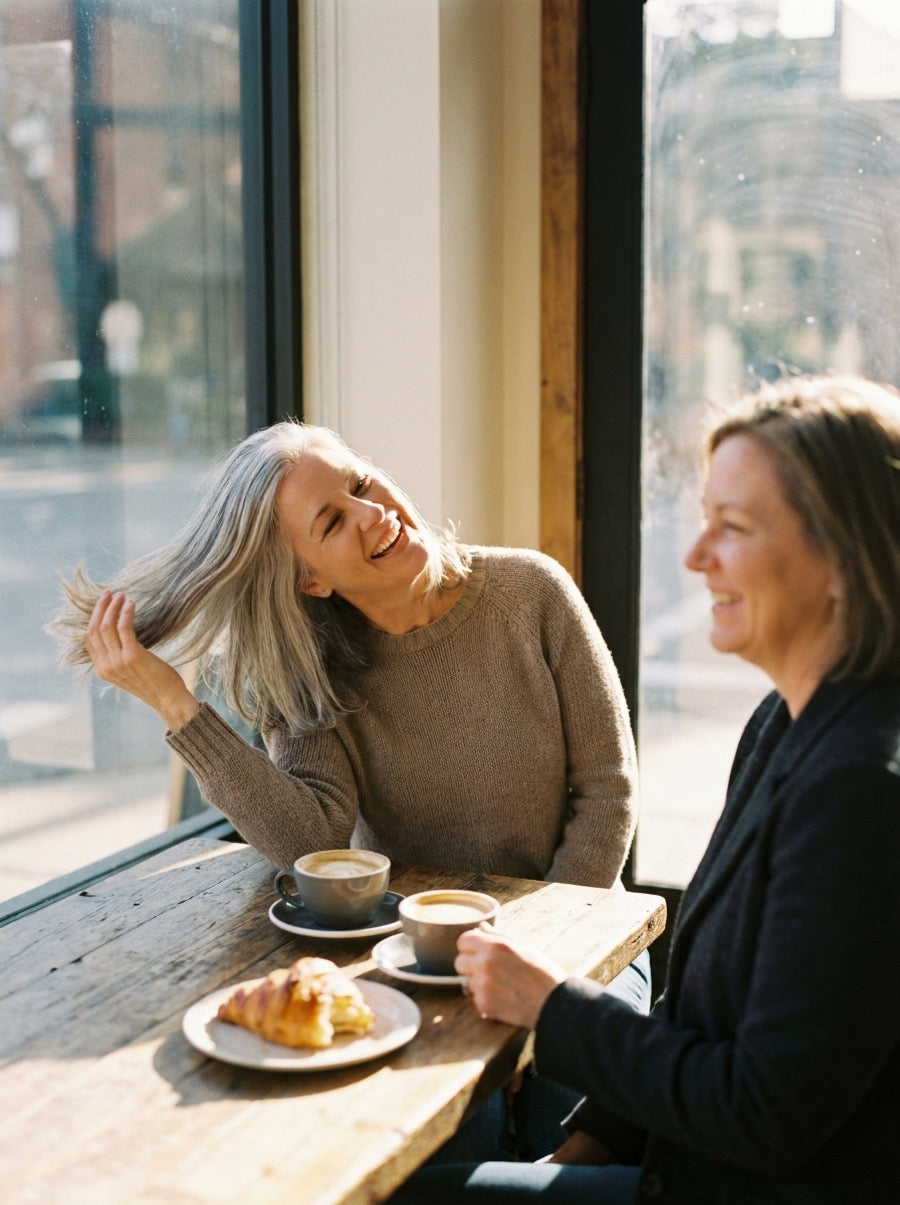 Silver-haired woman flipping her hair back laughing with a friend at a sunny cafe