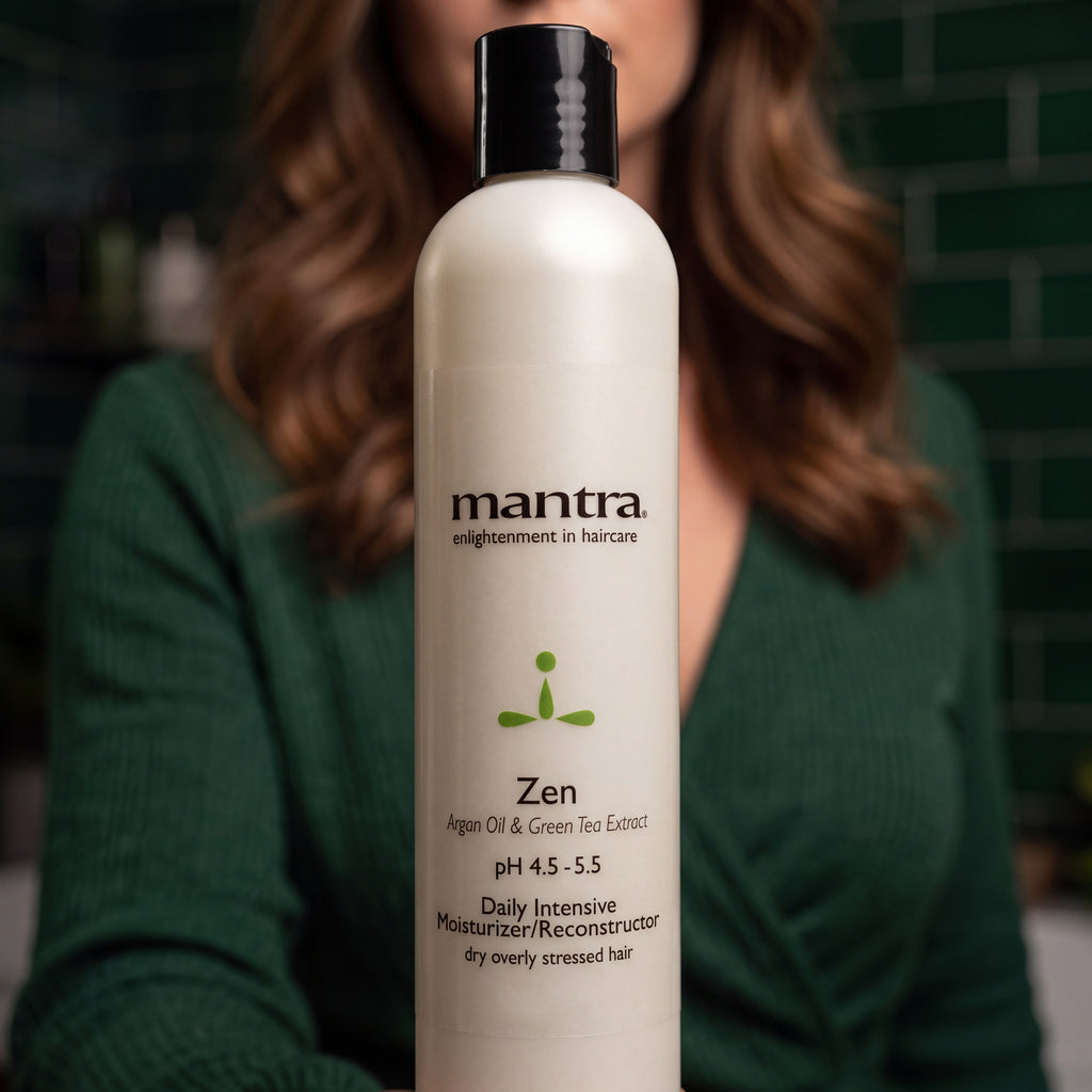 Woman in a forest green wrap top holding a bottle of Mantra Zen Intensive Reconstructor up to the camera in a dark green spa bathroom